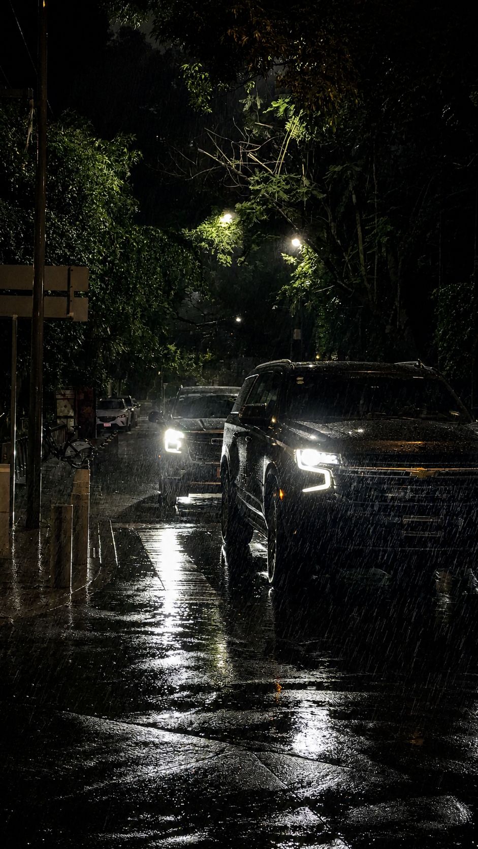 Dos camionetas negras circulan de noche sobre una calle mojada por la lluvia.